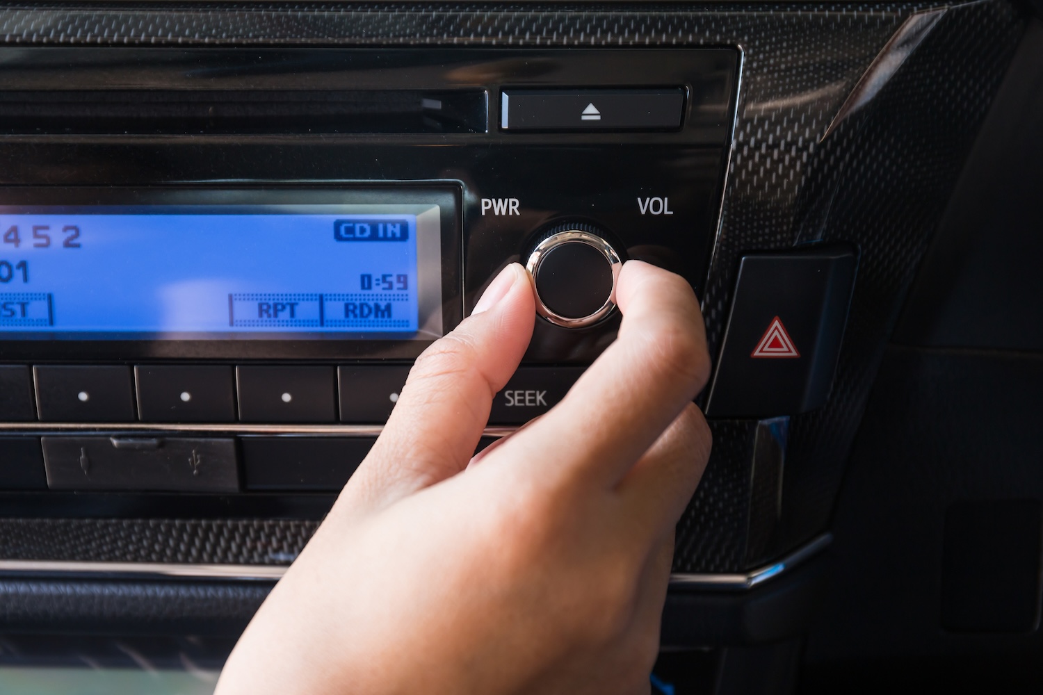 A hand turning the dial on a car stereo and auto radio replacement